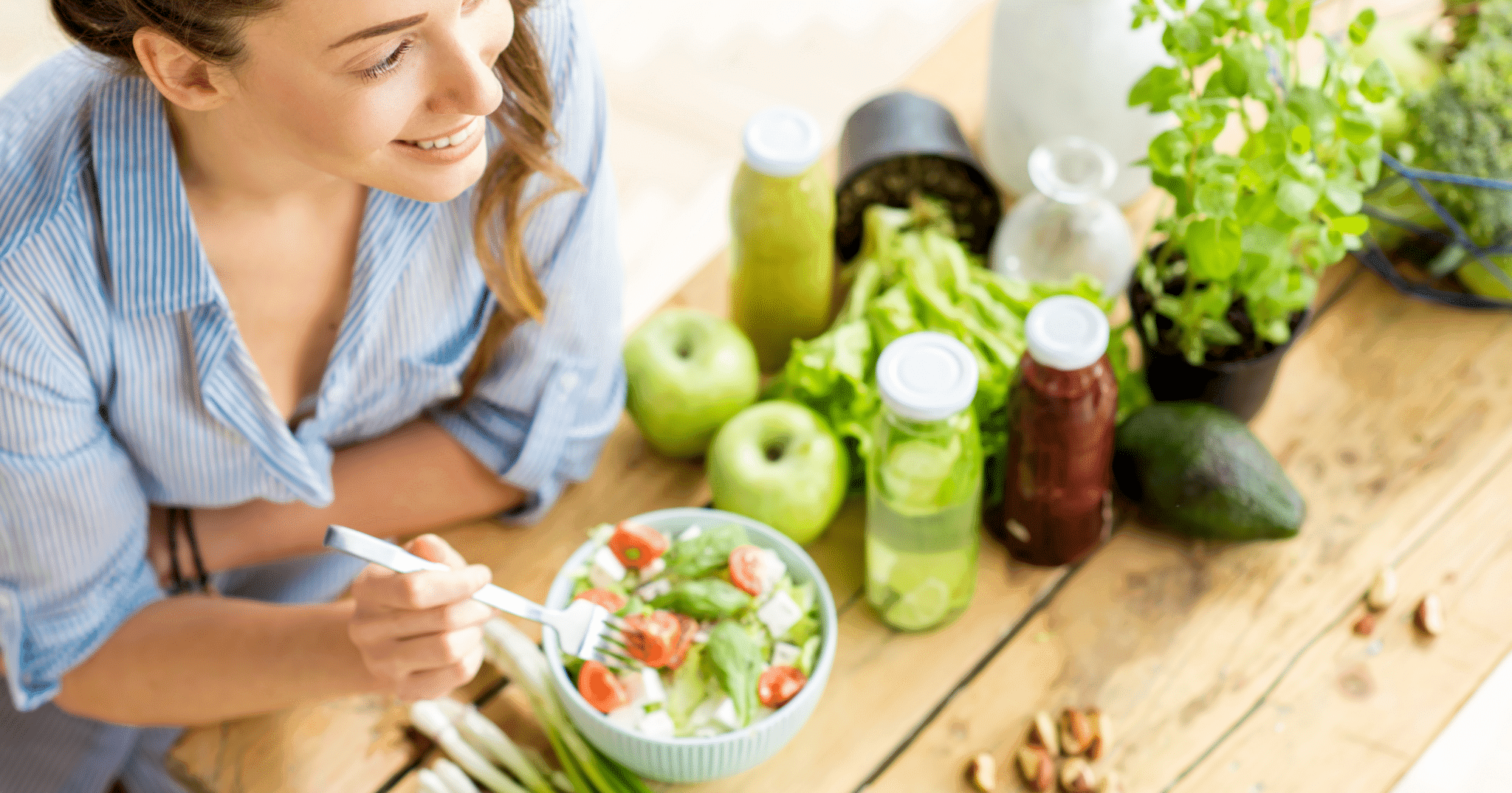 A woman enjoying a salad beside fresh vegetables and fruit